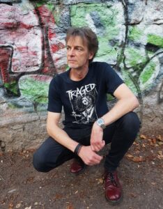 Uwe Roesch kniet vor eine Mauer mit Graffiti
