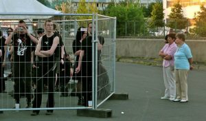 Gothics stehen hinter einem Zaun und werden von Passanten beobachtet.