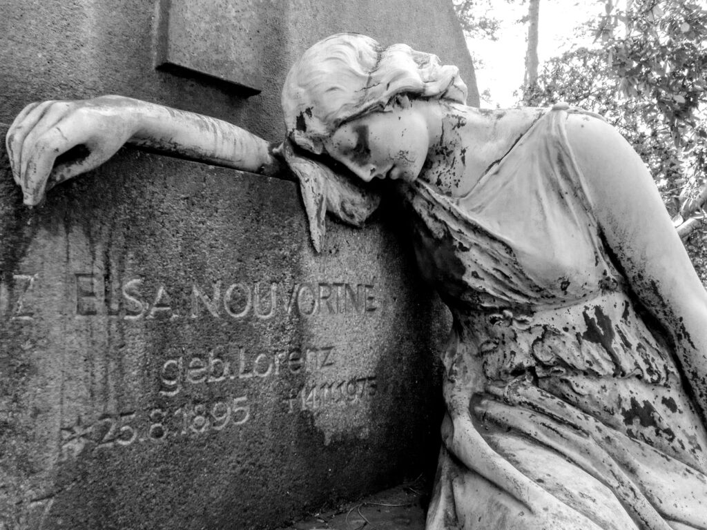 Frauenskulptur lehnt trauernd an Grabstein mit Inschrift