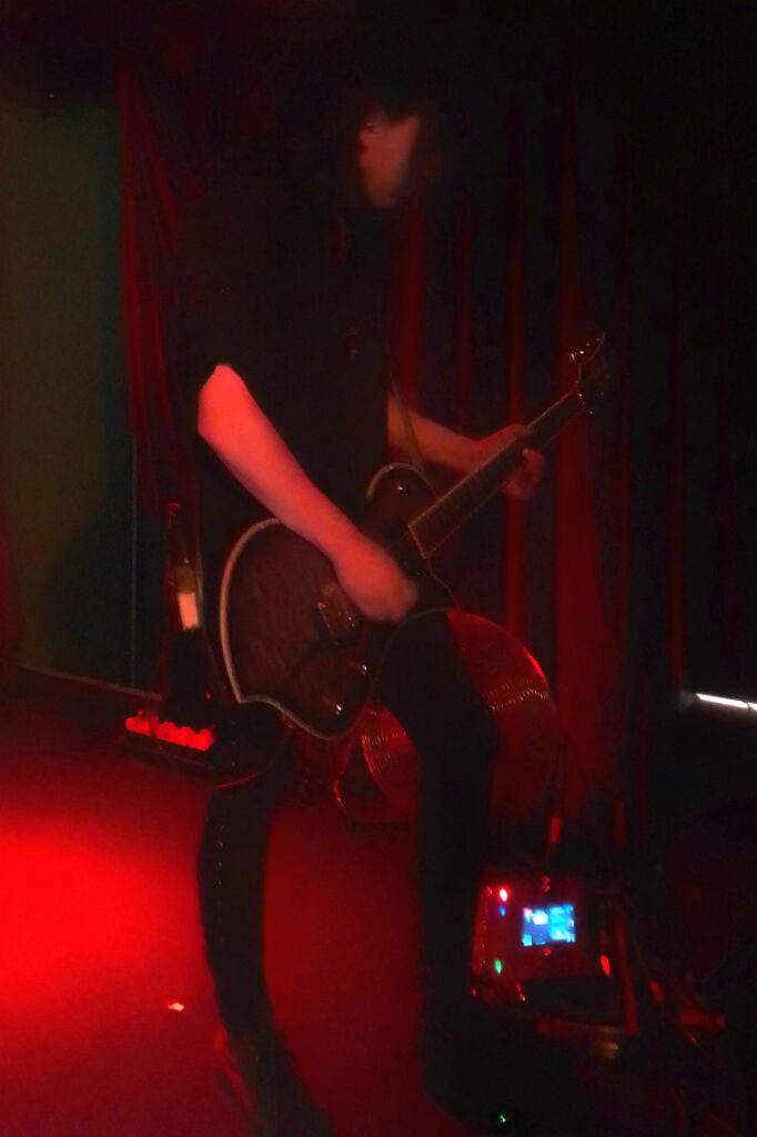 Gitarrist spielt elektrische Gitarre auf einer Bühne mit rotem Licht.