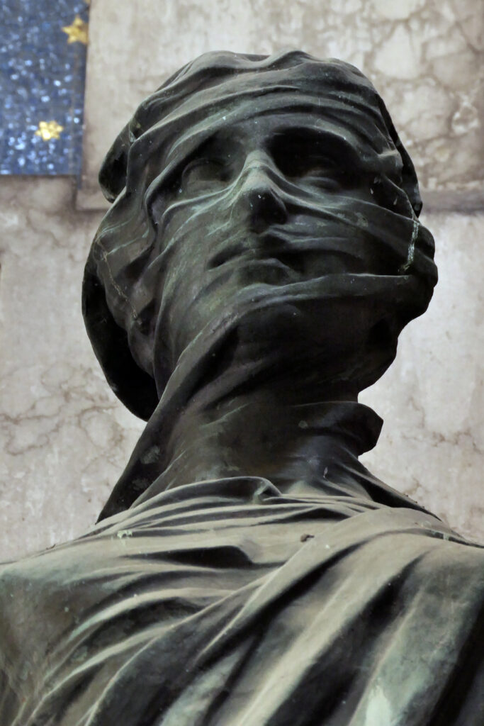 Bronzestatue eines bedeckten Kopfes mit dramatischer Stoffdrapierung.
